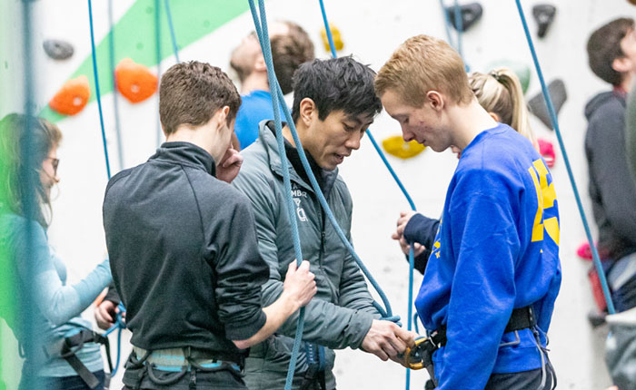 Climbing instructor showing climbers how to tie in to rope