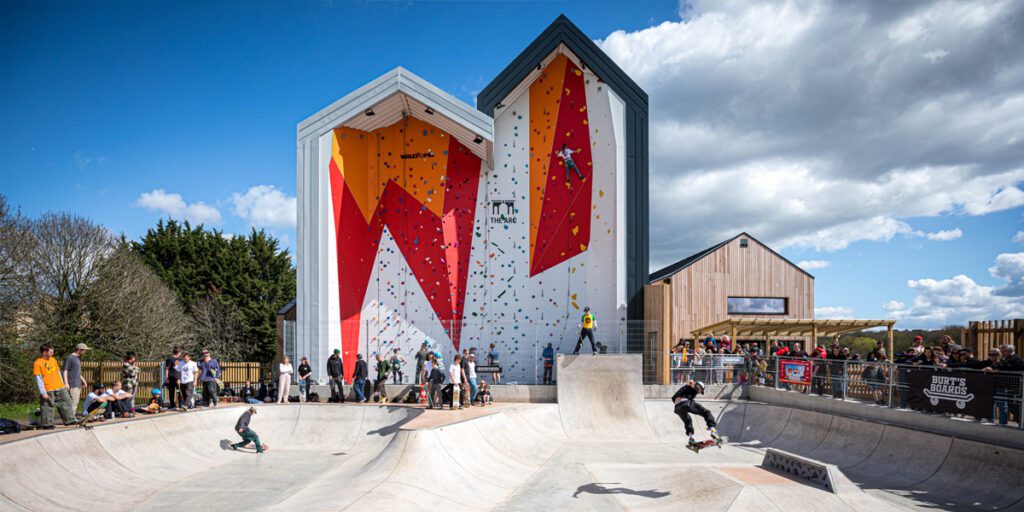 A wide photo showing the exterior of The Arc, including an outside climbing wall and a busy skatepark