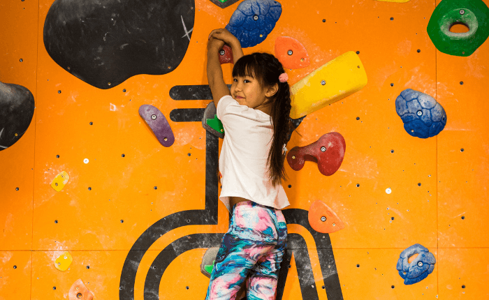 A young girls with pigtails holds on to a climbing wall while looking round and smiling