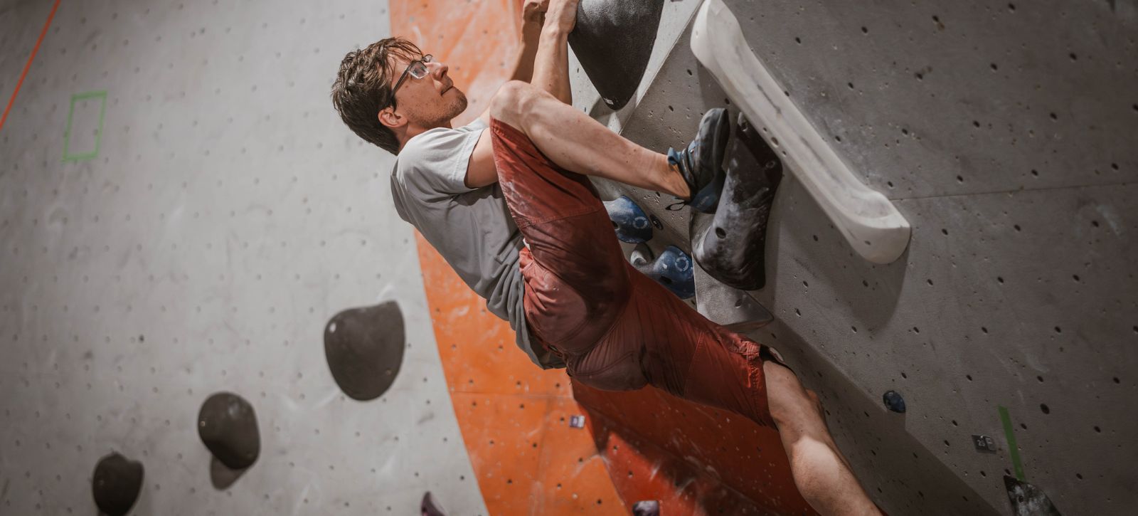 A man steps up very high while bouldering. He holds a sloper
