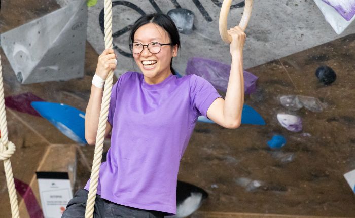 A lady grins while holding onto a rope in one hand and a gymnastic ring in the other