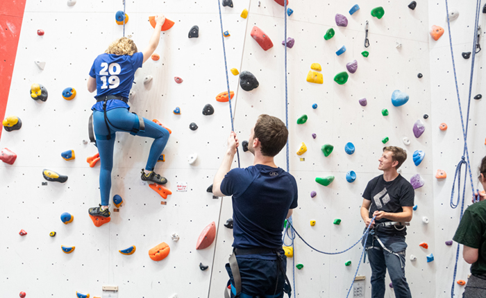 A coach helps someone to climb while someone else learns to belay.