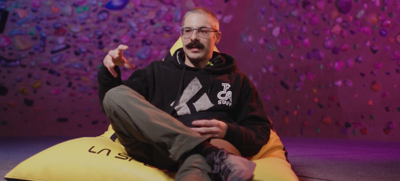 Ross Hunter sits on a bean bag in front of a climbing wall lit purple