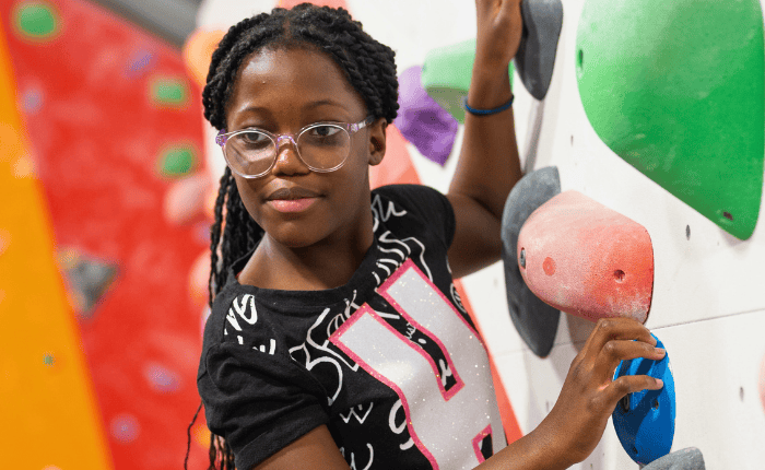 A young girl looks back while climbing on colourful holds