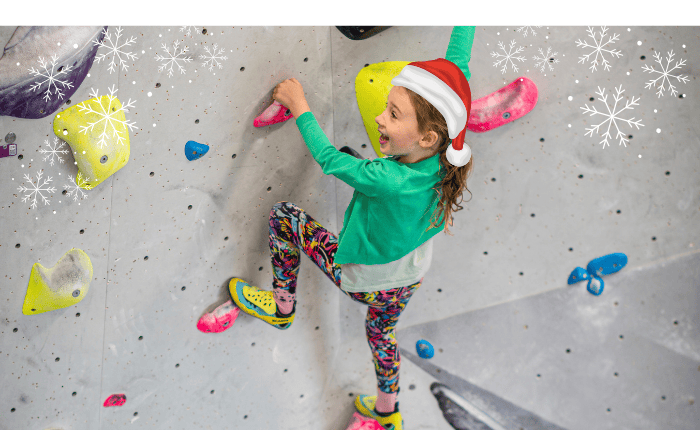 A little girls smiles as she climbs with a Christmas hat on. There are also some snowflake designs in the corners