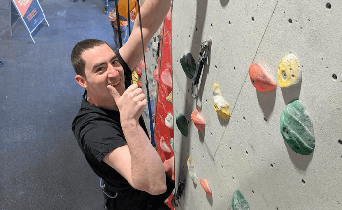 A man gives. thumbs up as he climbs on an auto belay
