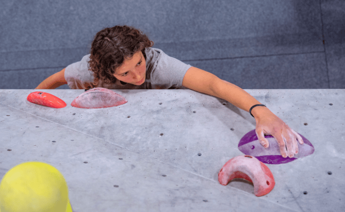 A climber is photographed from above, reaching up to their next hold.