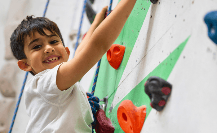 A child smiles as the camera while he rope climbs