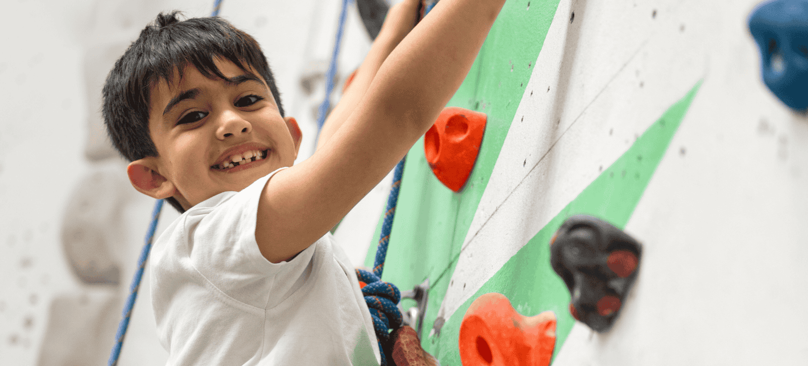 A child smiles as the camera while he rope climbs