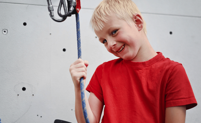 We see a young boy shyly smiling while he holds a rope.