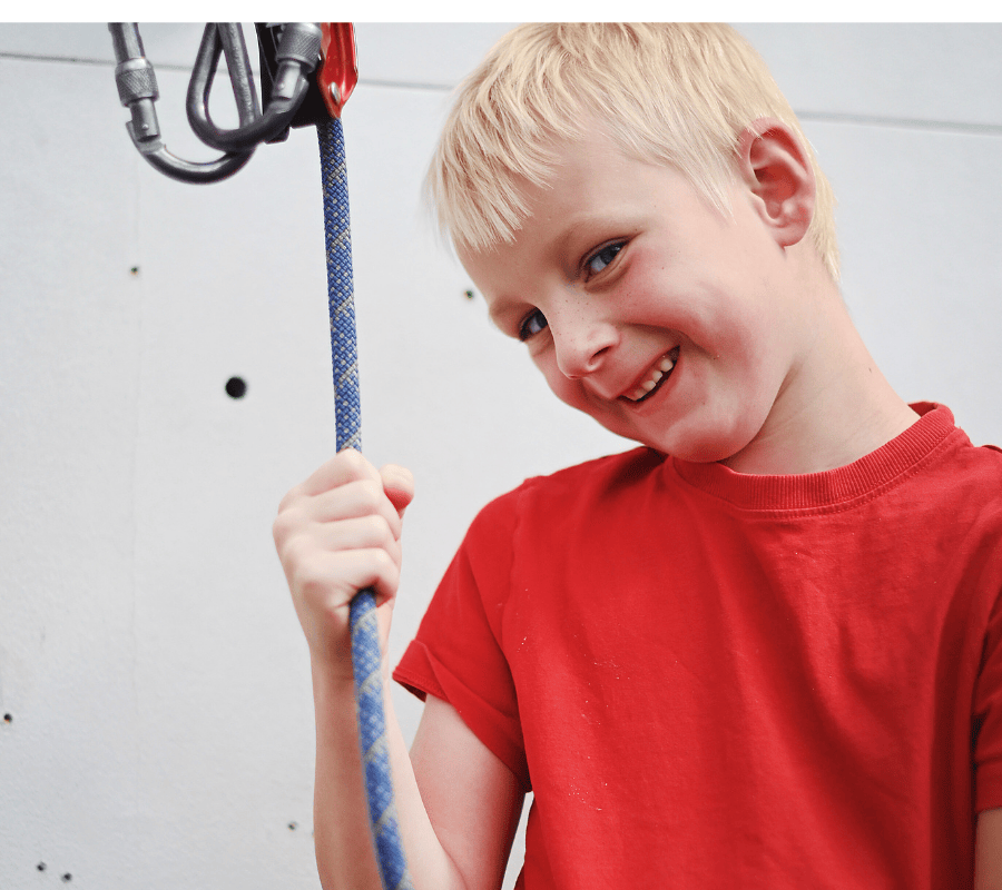 We see a young boy shyly smiling while he holds a rope.