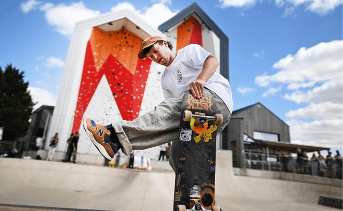 A skateboarder does a trick in the skatepark in front of the outdoor climbing wall at The Arc - whilst being watched by spectators.