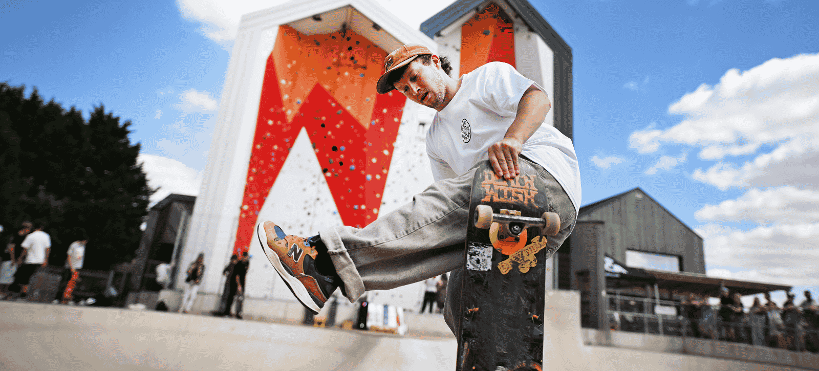 A skateboarder does a trick in the skatepark in front of the outdoor climbing wall at The Arc - whilst being watched by spectators.