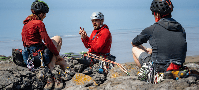 A climbing instructor talks to climbers at the top of a trad route on real rock