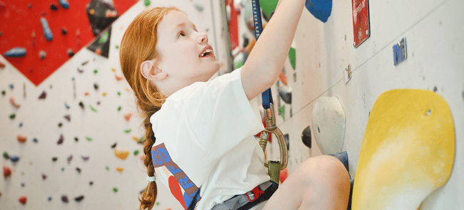 A child smiles as she looks up whilst rope climbing