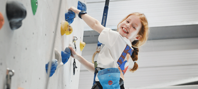 A child grins as she climbs on an auto belay